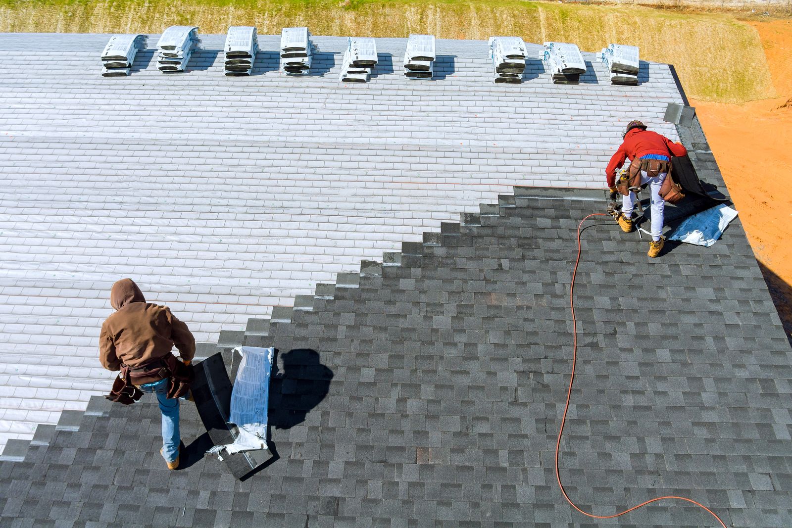 Roofers installing asphalt shingles on a home, with new shingle bundles staged across the ridge.
